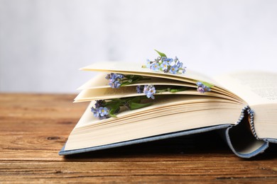 Photo of Beautiful forget-me-not flowers and book on wooden table against light background, closeup