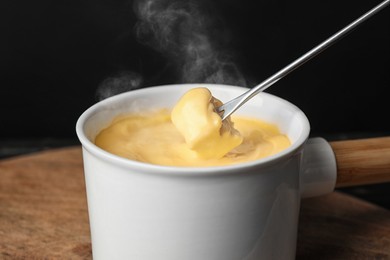 Image of Dipping piece of bread into fondue pot with tasty melted cheese at table, closeup