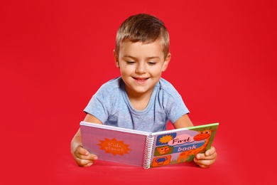 Photo of Cute little boy reading book on red background
