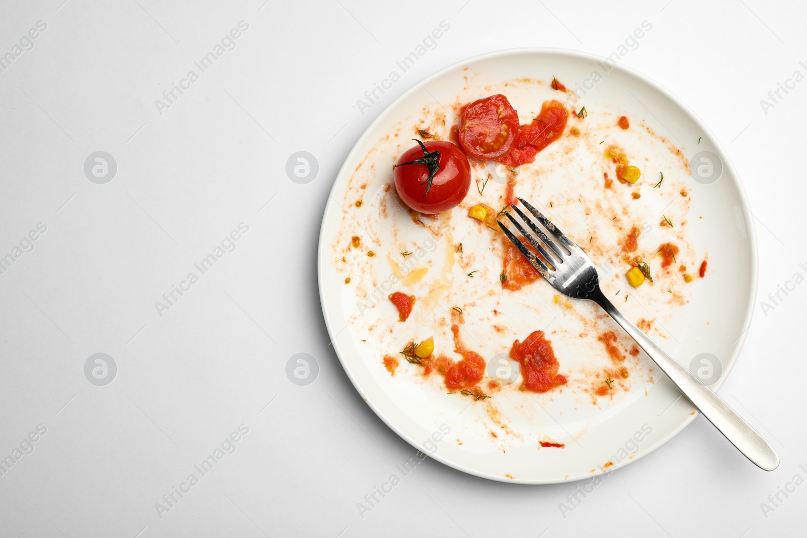 Photo of Dirty plate with food leftovers, tomato and fork on white background, top view