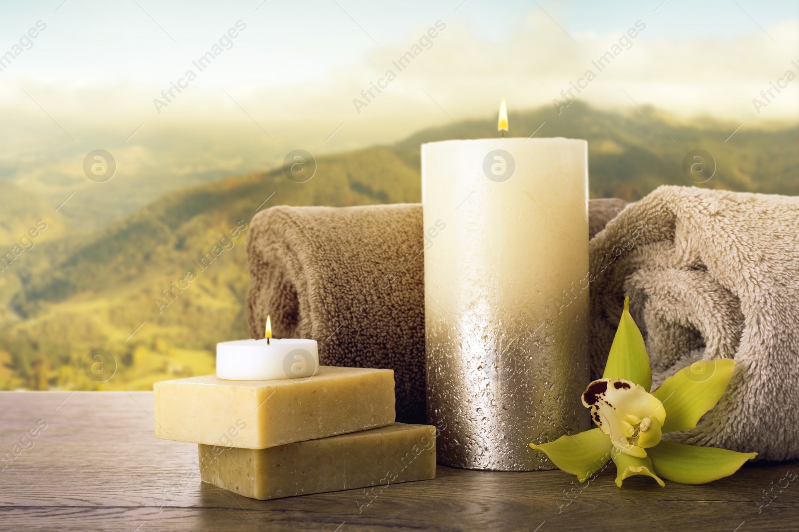Image of Spa holiday. Composition with towels, candle and soap bars on wooden table against beautiful mountain landscape