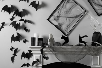 Black frames with cobweb on white wall, paper bats and different Halloween decor on fireplace indoors