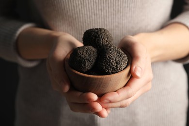 Photo of Woman holding wooden bowl of black truffles in hands, closeup