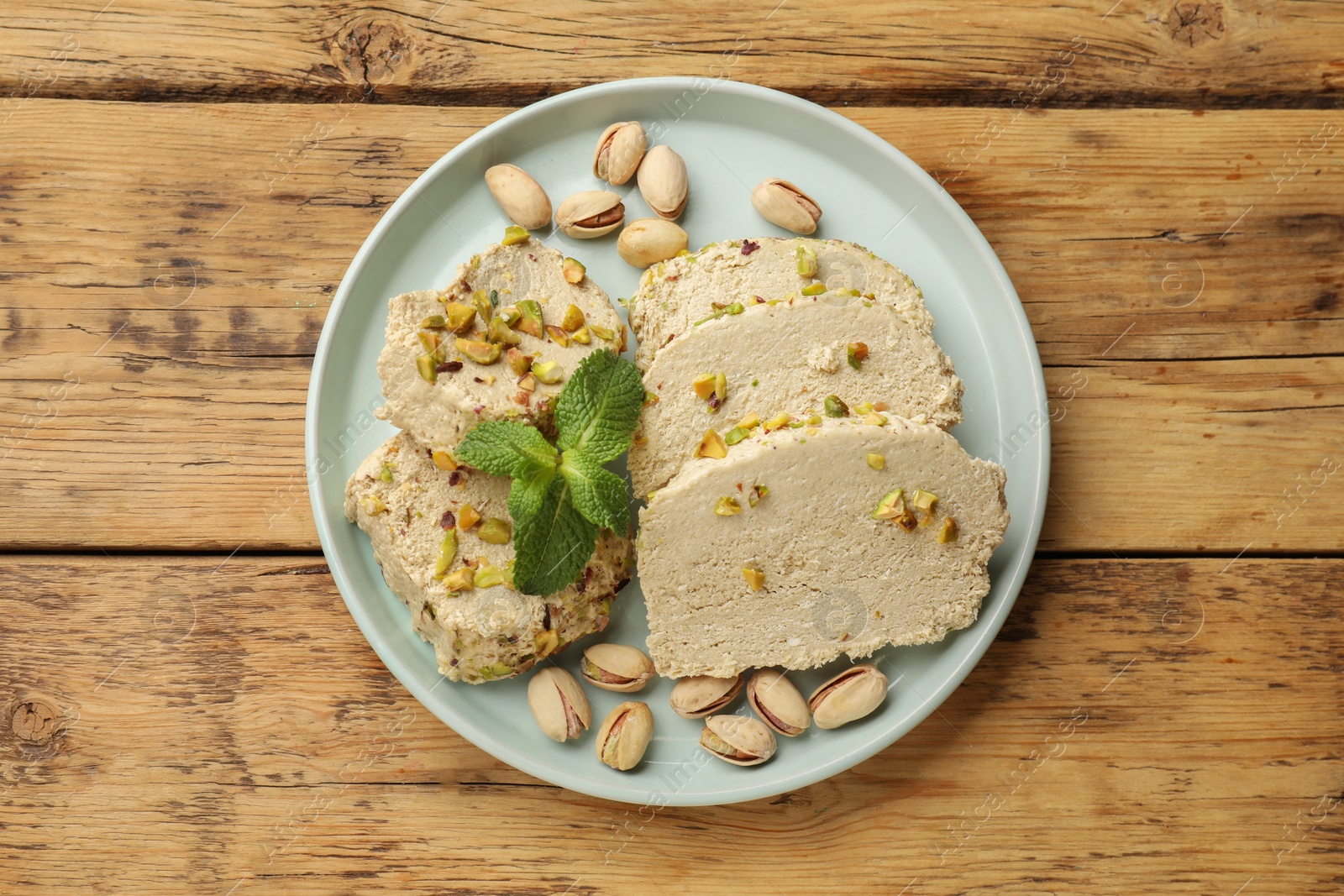 Photo of Tasty halva with pistachios and mint on wooden table, top view