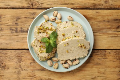 Photo of Tasty halva with pistachios and mint on wooden table, top view