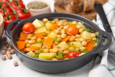 Tasty chickpea soup served on white tiled table, closeup