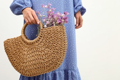 Woman holding beach bag with beautiful bouquet of wildflowers on white background, closeup