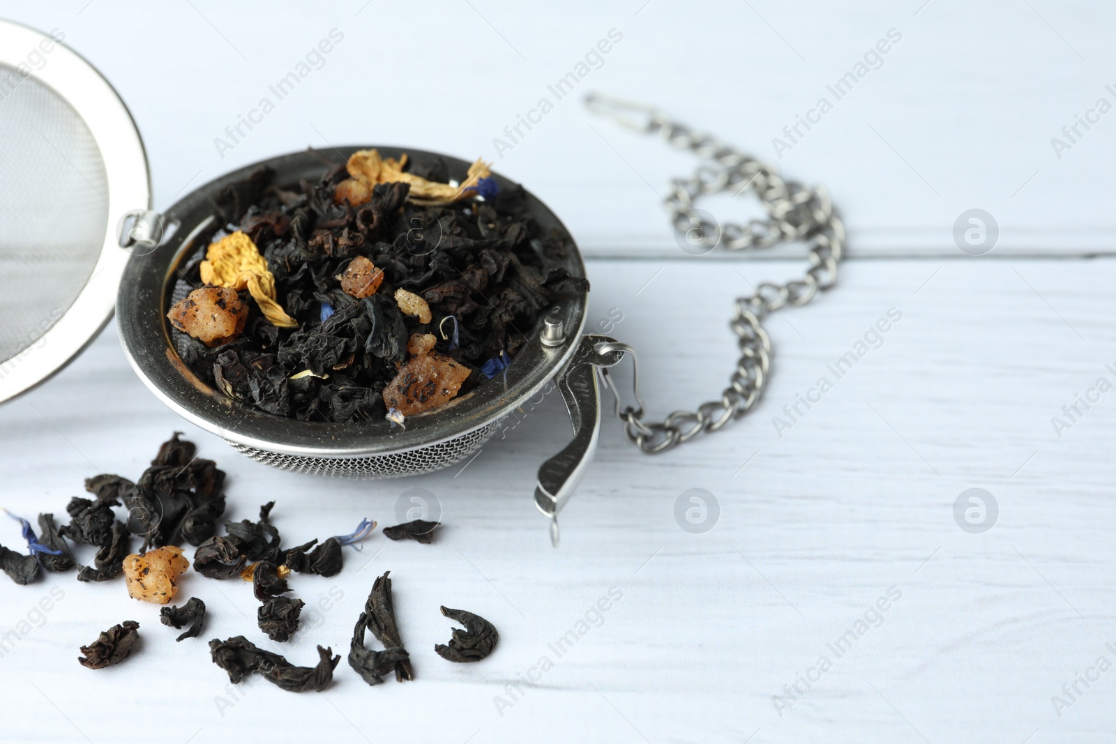 Photo of Snap infuser with dried herbal tea leaves on white wooden table, closeup. Space for text