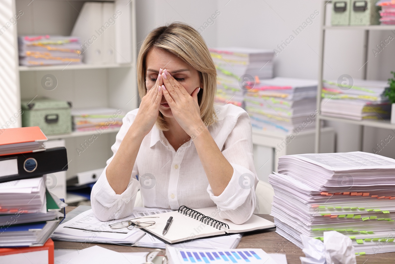 Photo of Overwhelmed woman surrounded by documents at workplace in office