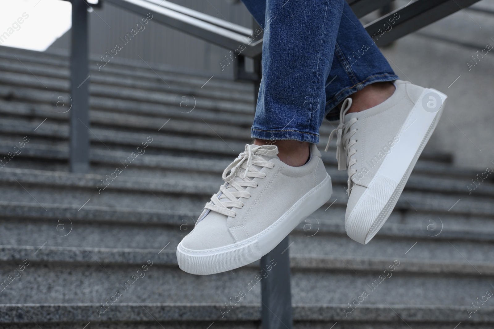 Photo of Man in stylish sneakers sitting on railing outdoors, closeup. Space for text