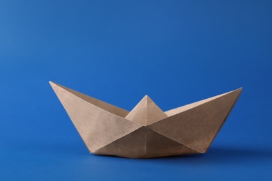 Photo of Handmade beige paper boat on blue background. Origami art