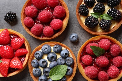 Tartlets with different fresh berries on grey table, flat lay. Delicious dessert