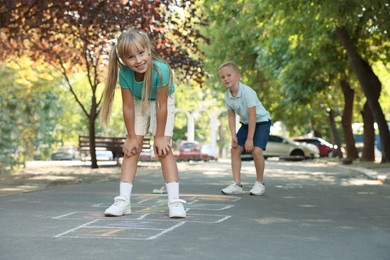 Photo of Little children playing hopscotch drawn with chalk on asphalt outdoors