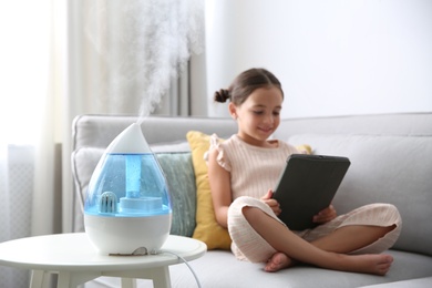 Little girl using tablet in room with modern air humidifier