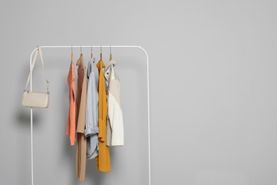 Photo of Rack with stylish women's clothes on wooden hangers and bag against light grey background, space for text