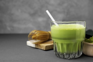 Photo of Glass of tasty matcha smoothie with straw on grey wooden table, closeup. Space for text