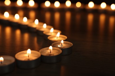 Photo of Burning candles on wooden table in darkness, closeup. Space for text