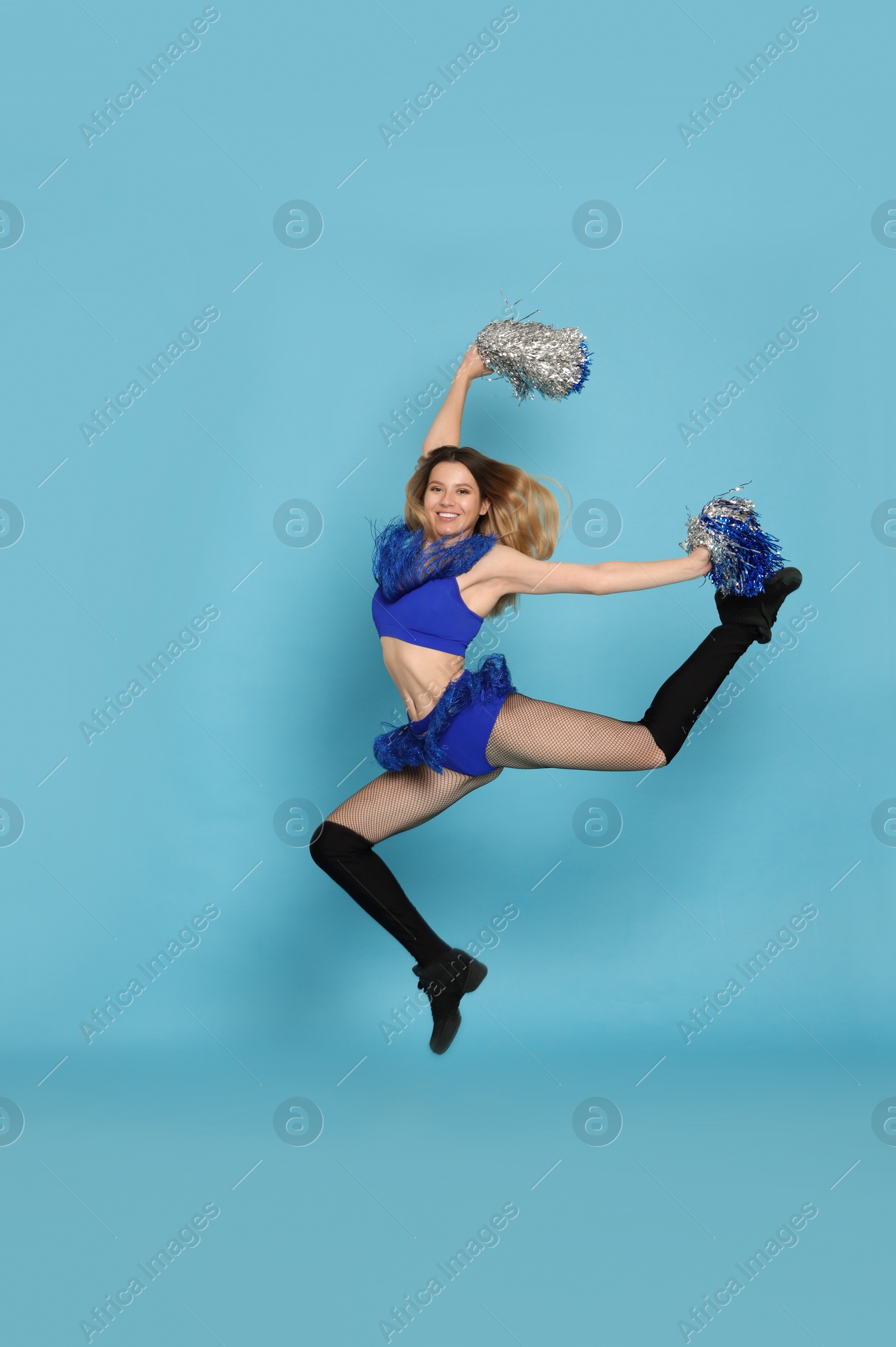 Photo of Beautiful cheerleader with pom poms jumping on light blue background