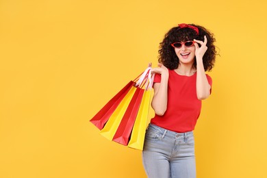 Photo of Happy young woman with shopping bags and stylish sunglasses on yellow background. Space for text