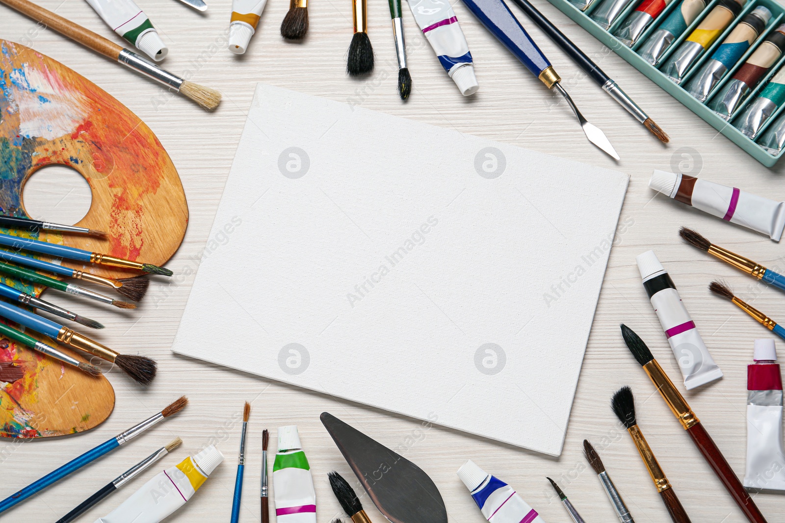 Photo of Blank canvas, brushes, paints and palette on white wooden table, flat lay. space for text