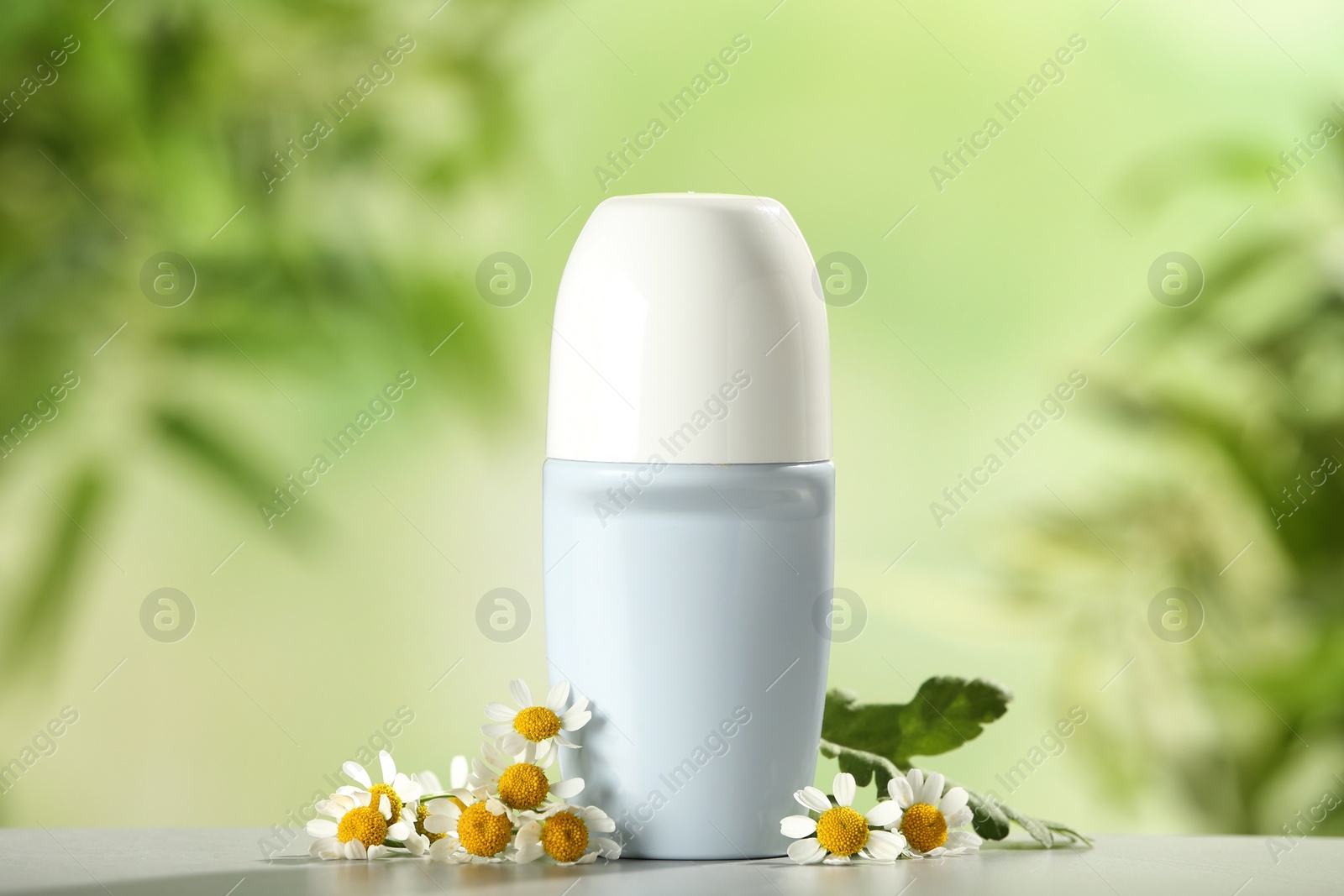 Photo of Deodorant container and chamomile on white wooden table against blurred background