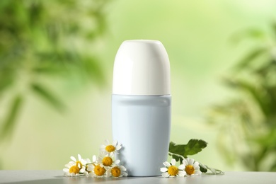 Photo of Deodorant container and chamomile on white wooden table against blurred background