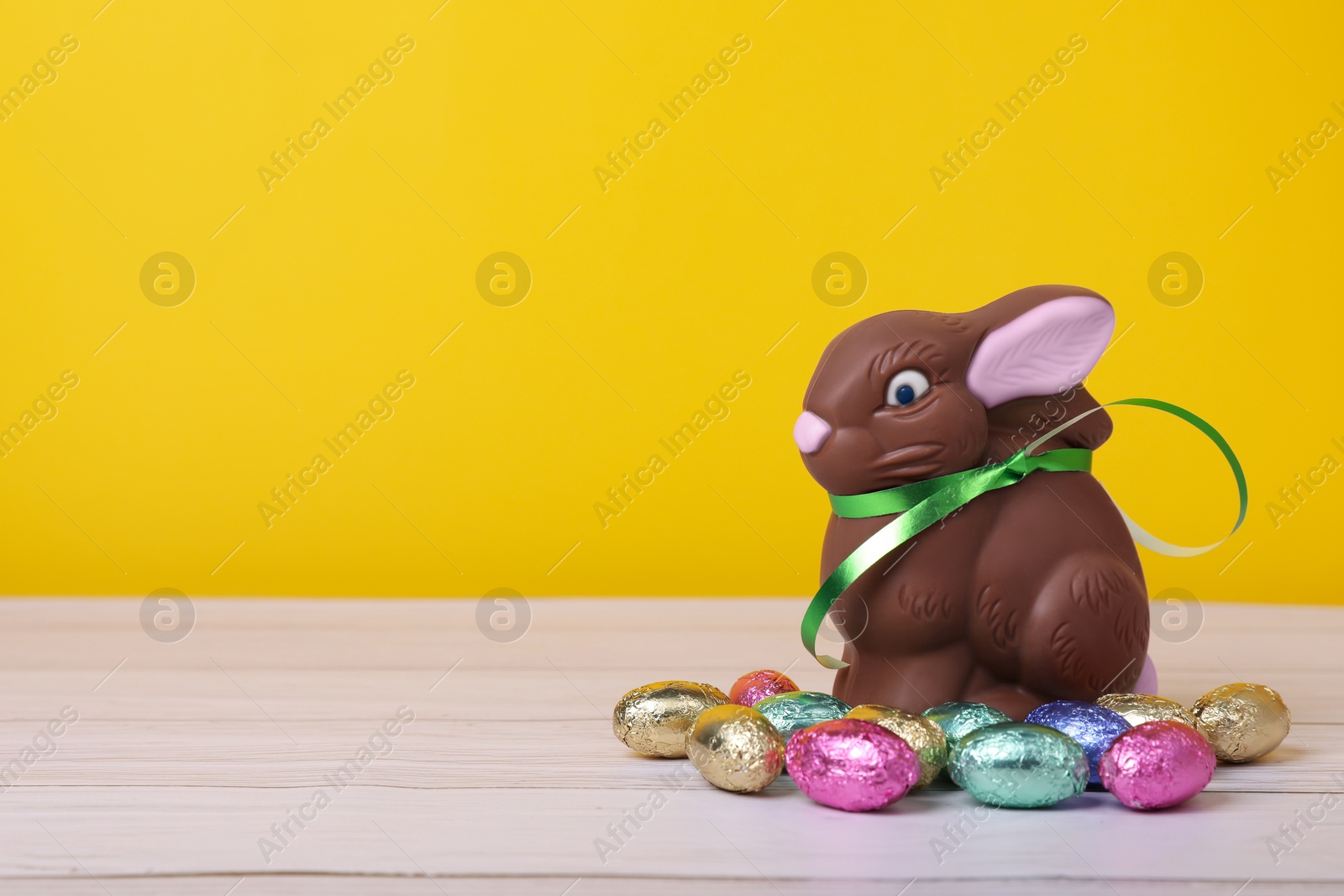 Photo of Chocolate Easter bunny and eggs on white wooden table against yellow background. Space for text