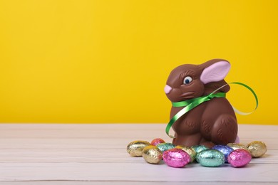 Chocolate Easter bunny and eggs on white wooden table against yellow background. Space for text