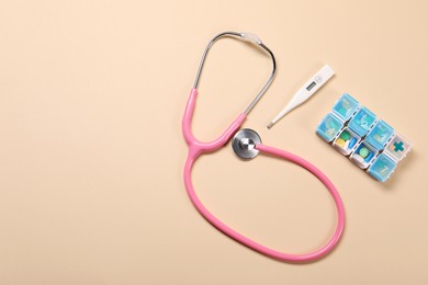 Stethoscope, thermometer and pills on beige background, flat lay. Space for text