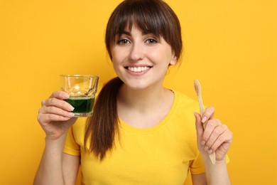 Young woman with mouthwash and toothbrush on yellow background