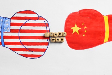 Photo of Wooden cubes with words Trade War, boxing gloves with American and Chinese flags drawn on white paper, top view