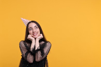 Photo of Happy woman in party hat on orange background, space for text