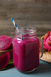 Photo of Delicious pitahaya smoothie in mason jar and fresh fruits on light blue wooden table, closeup