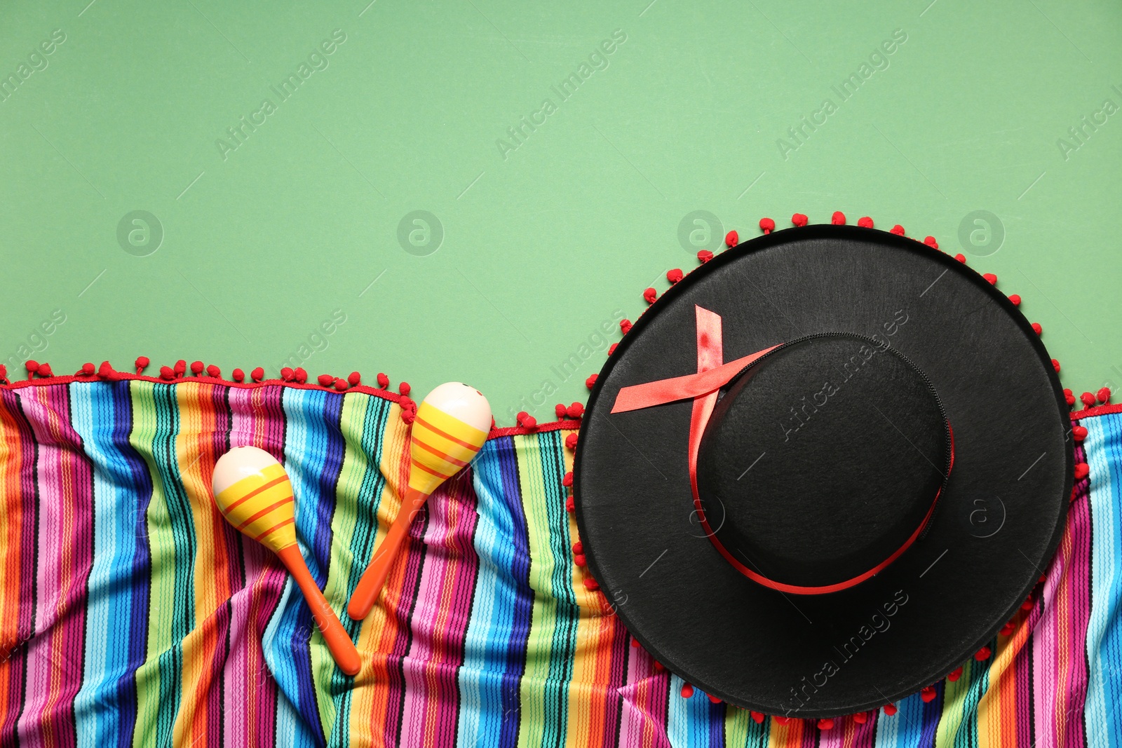 Photo of Mexican sombrero hat, maracas and colorful poncho on green background, flat lay. Space for text