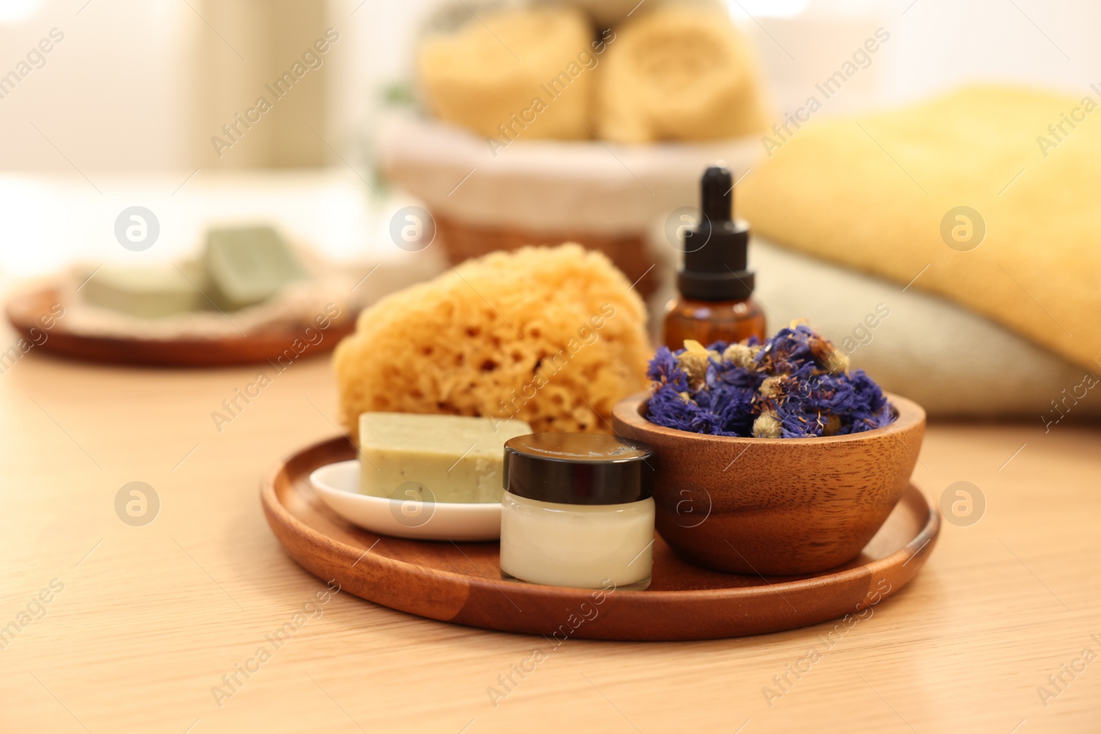 Photo of Dry flowers, loofah, soap bar, bottle of essential oil and jar with cream on wooden table indoors. Spa time