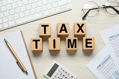 Cubes with words Tax Time, documents, keyboard, glasses and calculator on white wooden table, flat lay