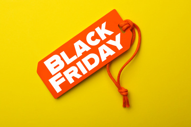 Tag with text BLACK FRIDAY on yellow background, top view