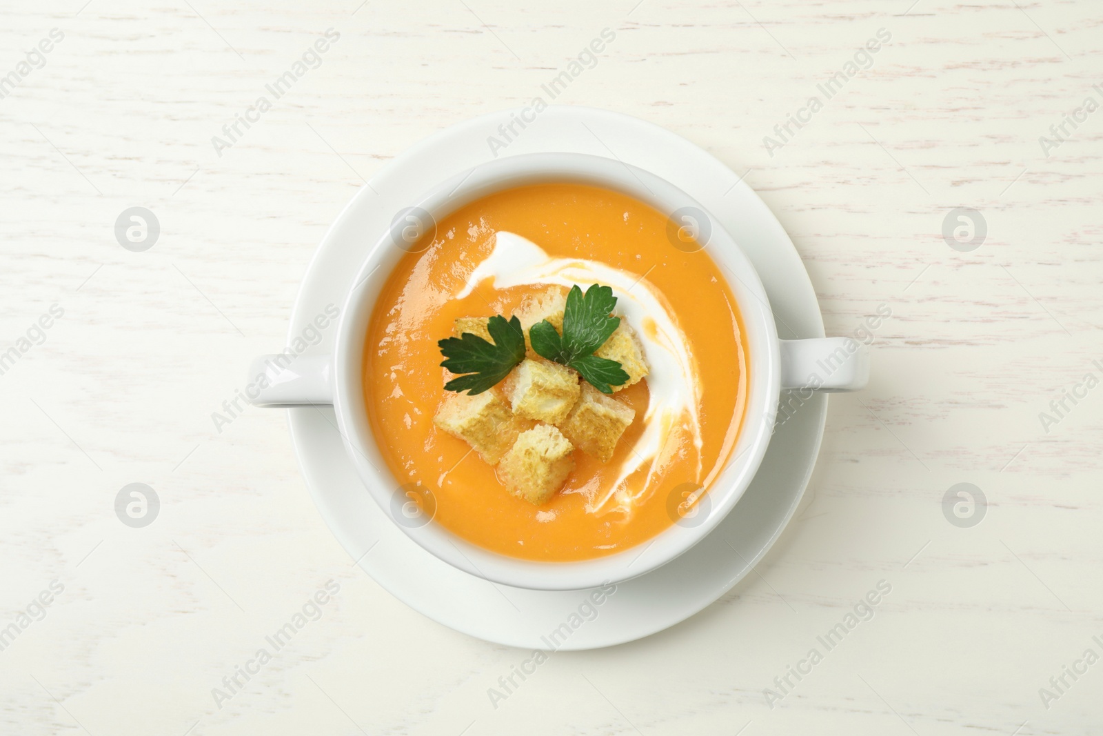 Photo of Delicious pumpkin soup in bowl on white wooden table, top view