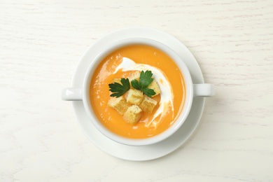 Photo of Delicious pumpkin soup in bowl on white wooden table, top view
