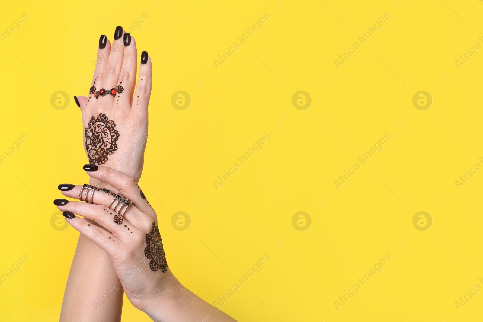 Photo of Woman with henna tattoos on hands against yellow background, closeup and space for text. Traditional mehndi ornament