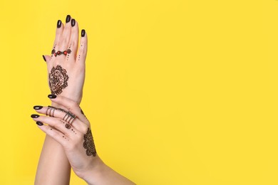 Photo of Woman with henna tattoos on hands against yellow background, closeup and space for text. Traditional mehndi ornament