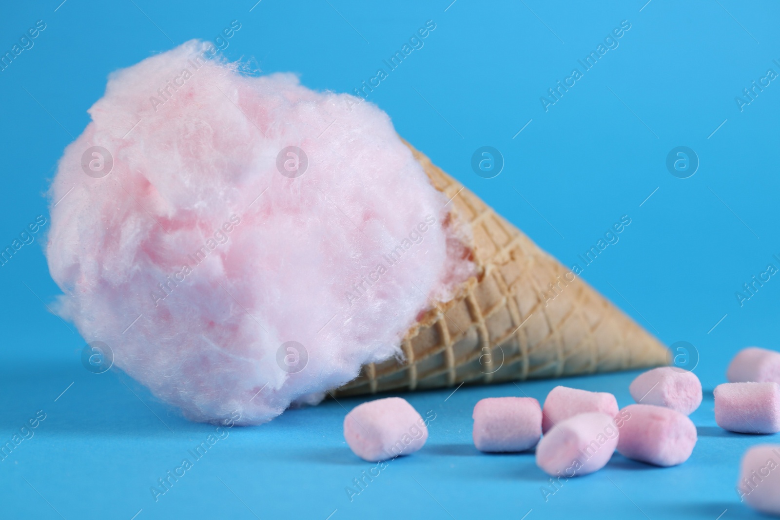 Photo of Sweet cotton candy in waffle cone and marshmallows on light blue background, closeup