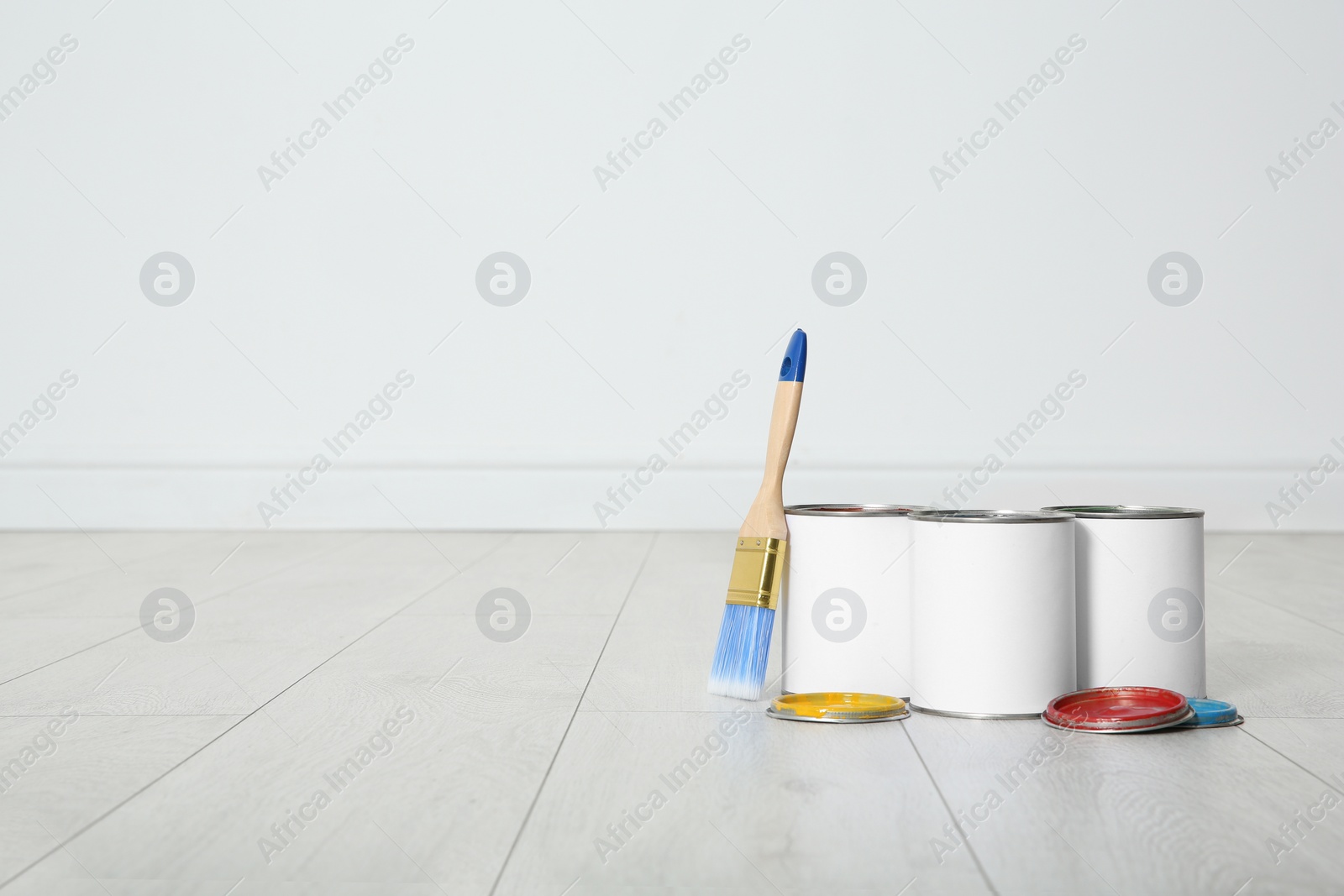 Photo of Cans of paint and brush on wooden floor indoors. Space for text