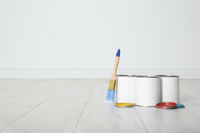 Cans of paint and brush on wooden floor indoors. Space for text