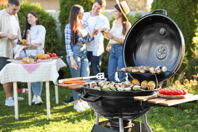 Photo of Group of friends having party outdoors. Focus on barbecue grill with food