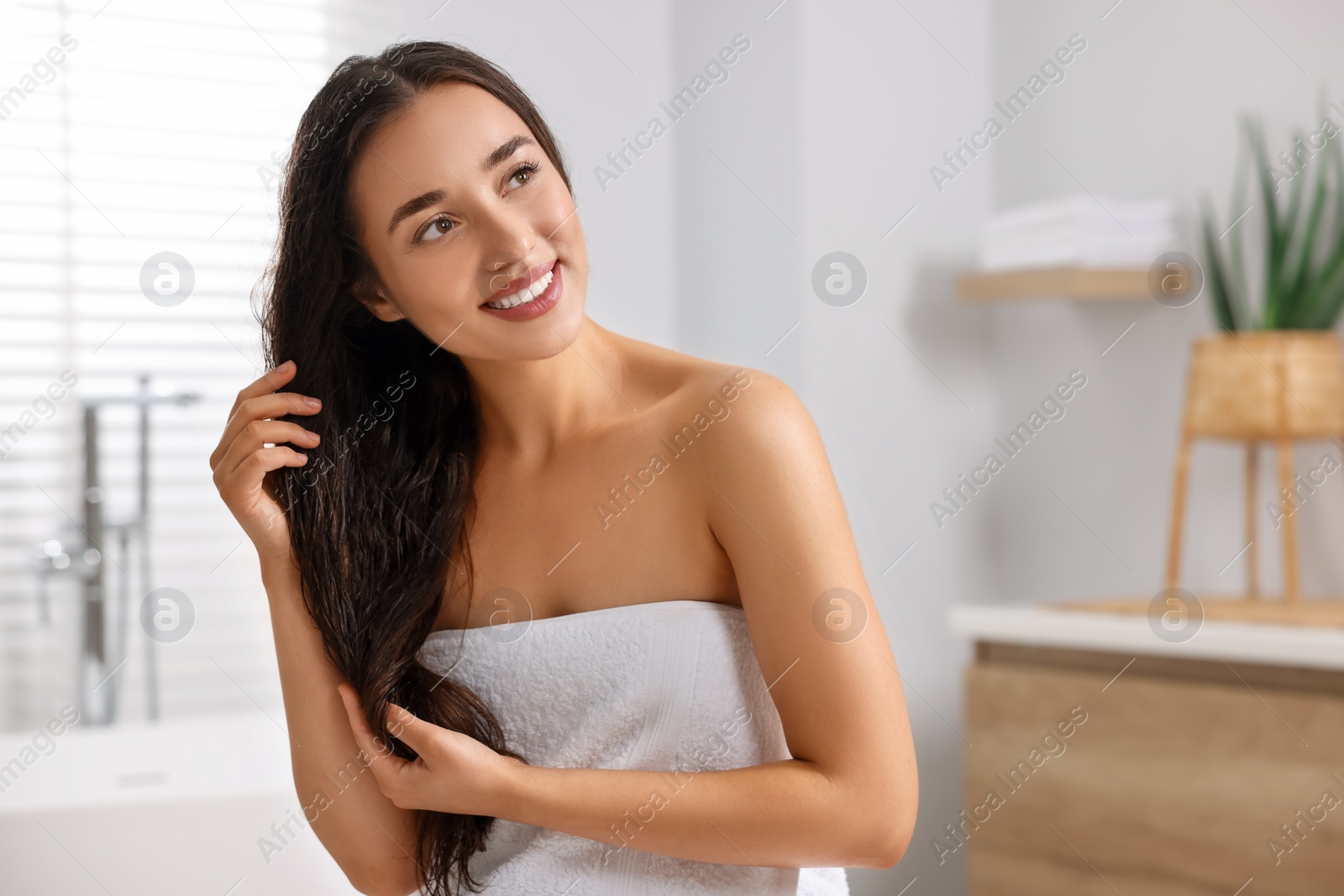 Photo of Young woman applying cosmetic hair mask in bathroom