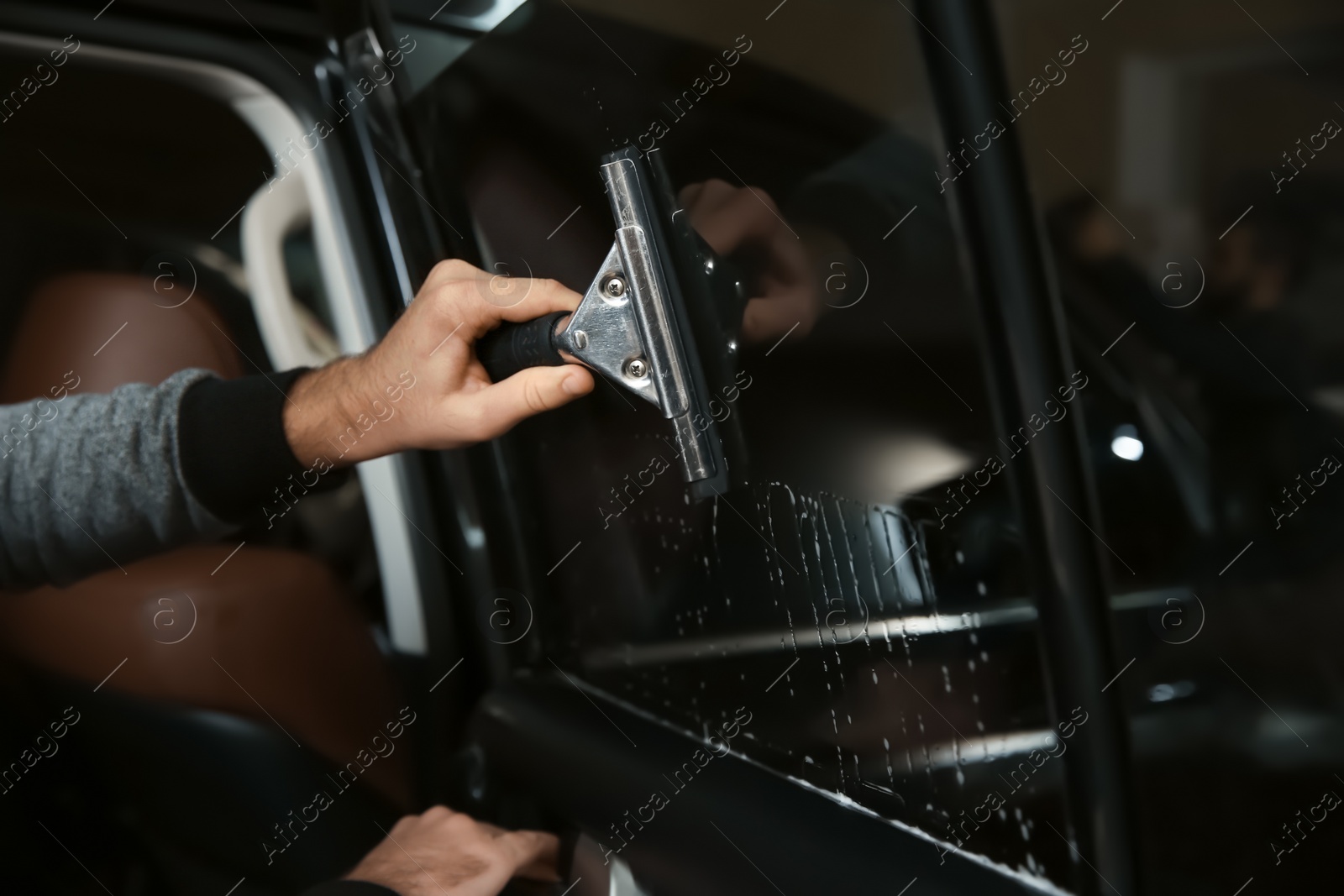 Photo of Worker washing car window before tinting in shop, closeup