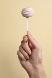 Woman holding sweet cake pop on light background, closeup