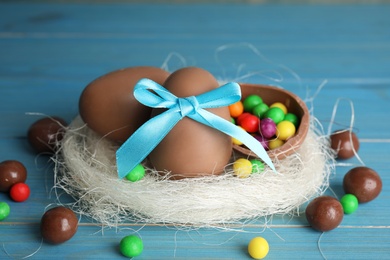 Photo of Composition with tasty chocolate eggs, colorful candies and decorative nest on light blue wooden table