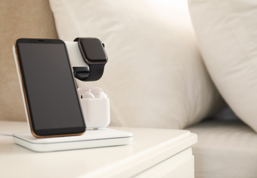Photo of Different gadgets charging on wireless pad in bedroom, closeup. Space for text